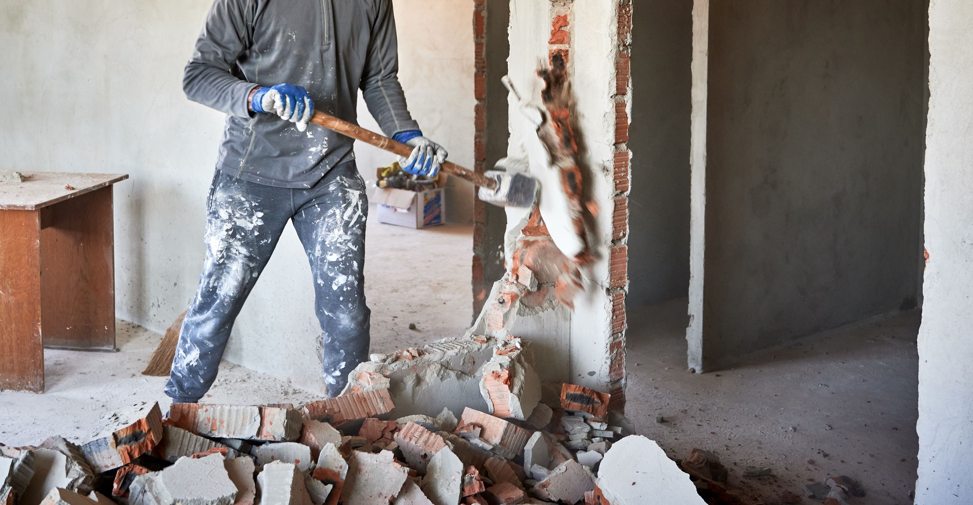 Cropped view dismantler crashing interroom septum with hand's large hammer.